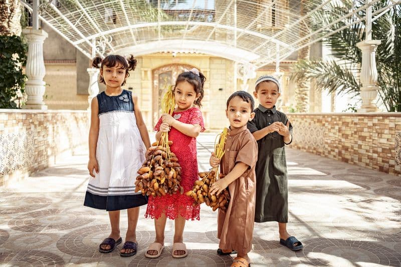 Kinder in traditioneller Kleidung mit frisch geernteten Dattelbüscheln